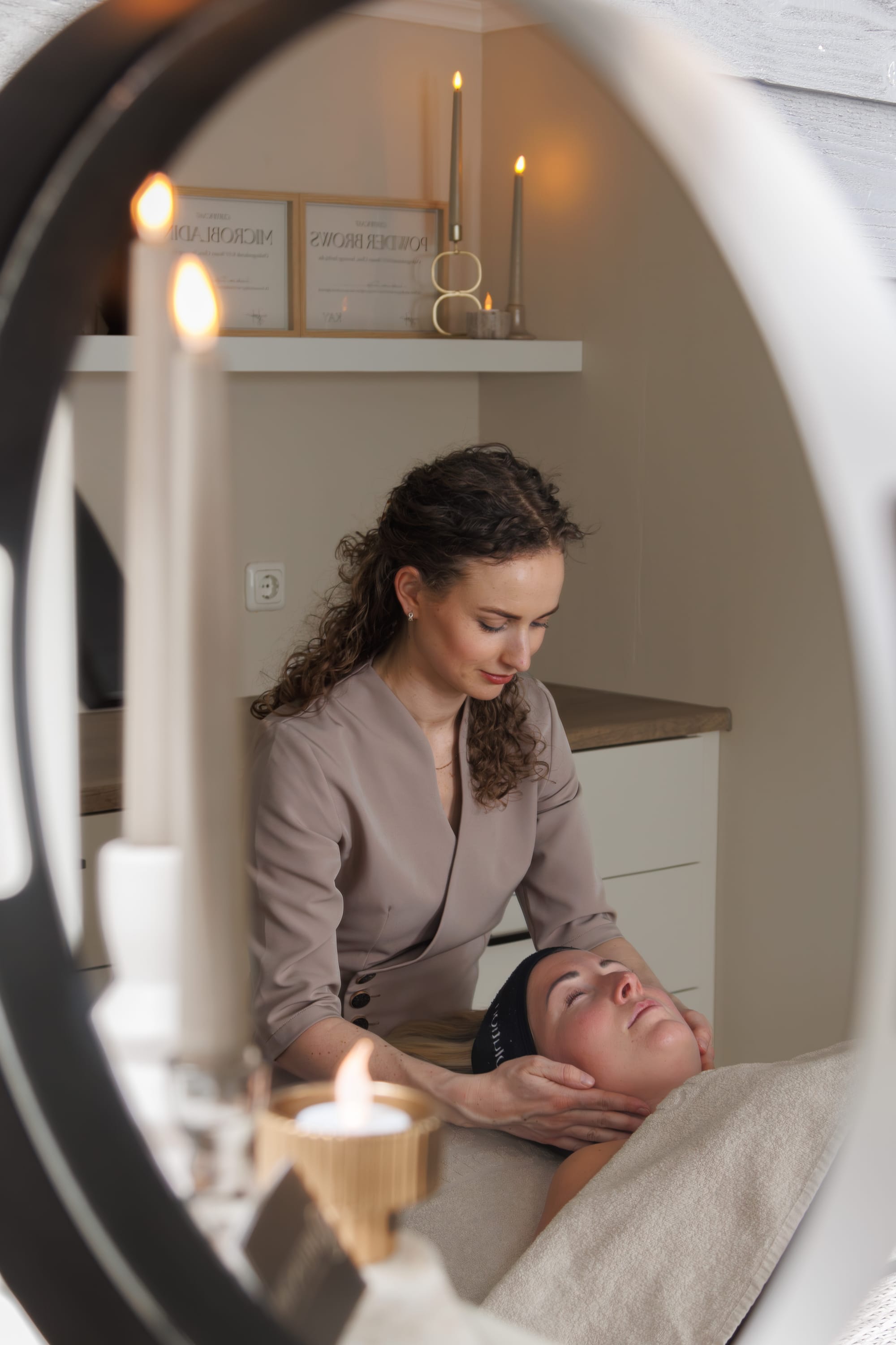 Behandelruimte weerspiegeld in de ringlamp, met kaarsen en de certificaten voor microblading en powder brows