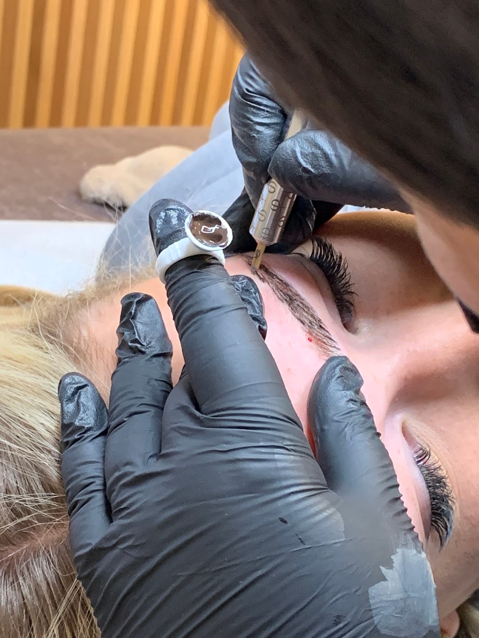 Permanente make-up wordt aangebracht: pigment in een ring en een PMU-pen langs de wenkbrauw